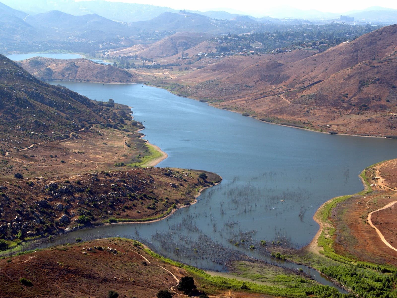 Aerial view of Lake Hodges winding between brown hills, with homes in the distance.