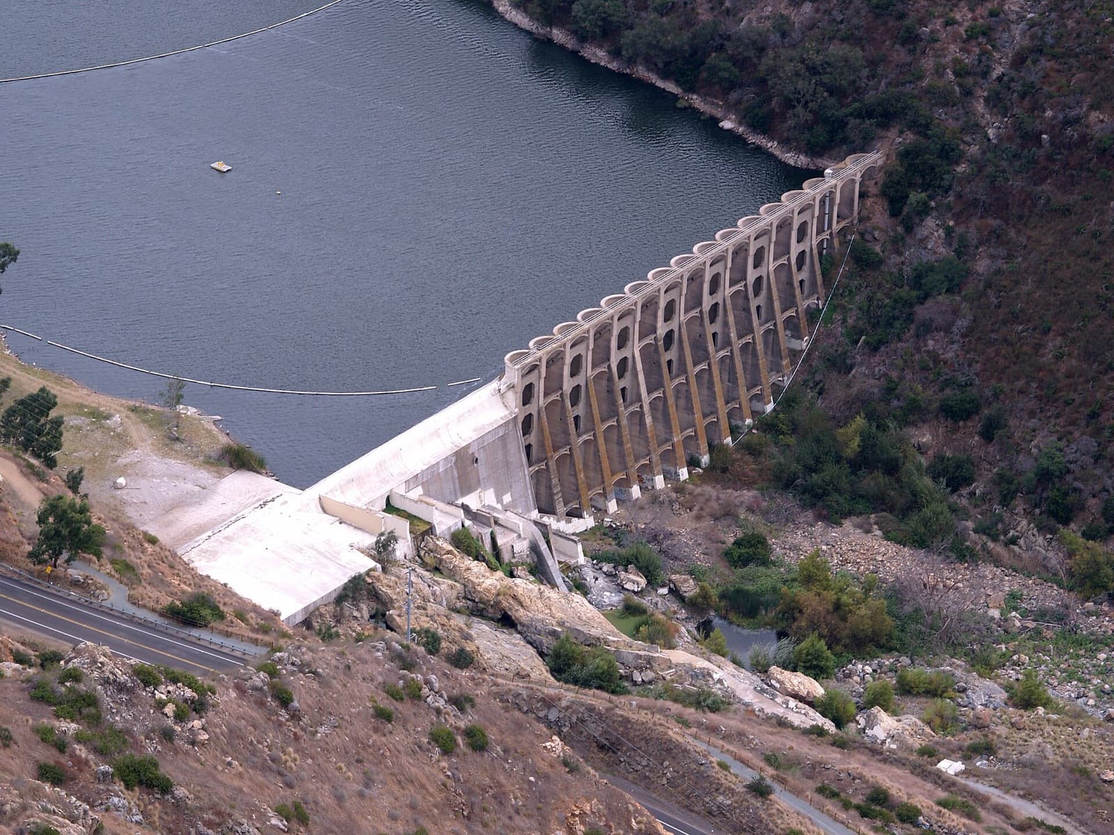 The concrete arched Lake Hodges Dam seen from above, with the reservoir behind it and a road at lower left.